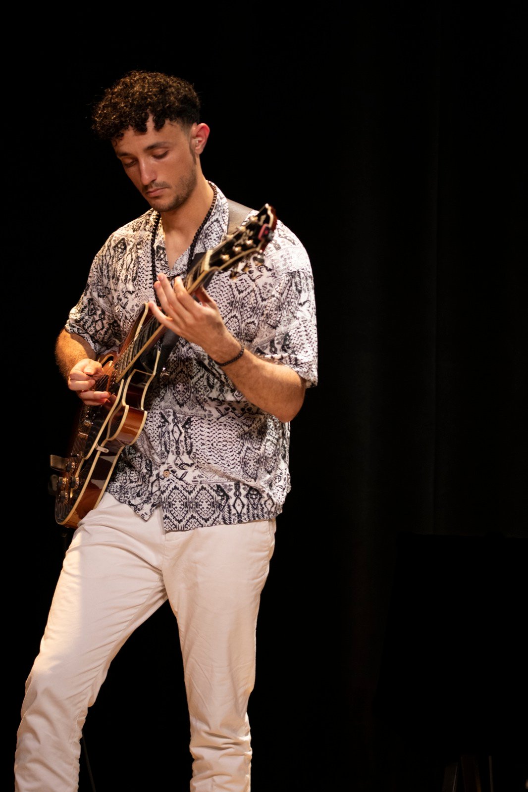 Lucas Baret standing at the front of a dark stage, playing the hollowbody archtop